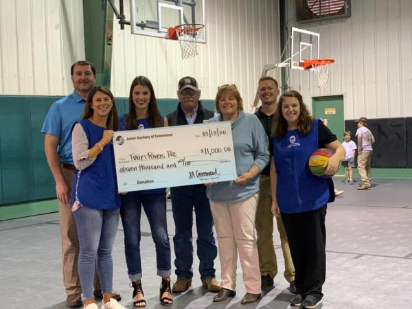 Junior Auxiliary members posing with a charity member with a large check. 