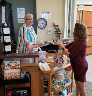 Two women at a hospital gift shop. One is paying for an item and the other is a volunteer who is smiling at the camera.